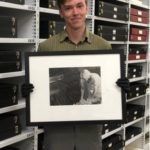 Summer 2022 intern Connor Smith holding a framed photograph in collection storage.