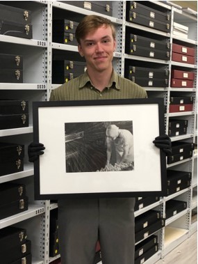 Summer 2022 intern Connor Smith holding a framed photograph in collection storage.
